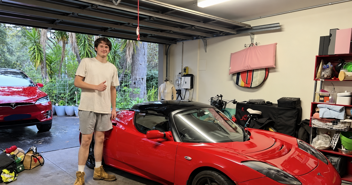 Jake from STIKKYS beside a red Tesla Roadster in a garage