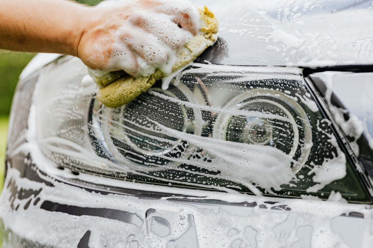 Hand washing a car headlight with a soft wash mitt during a mobile detail