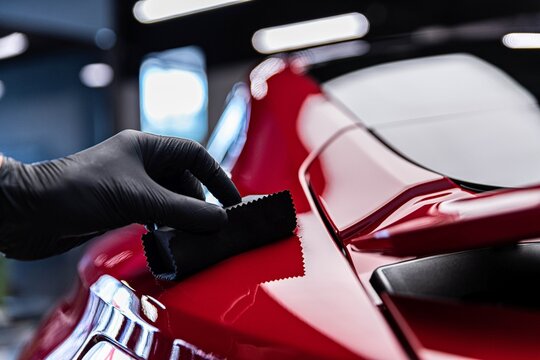 Gloved hand wiping red paint with an applicator cloth during a ceramic coating
