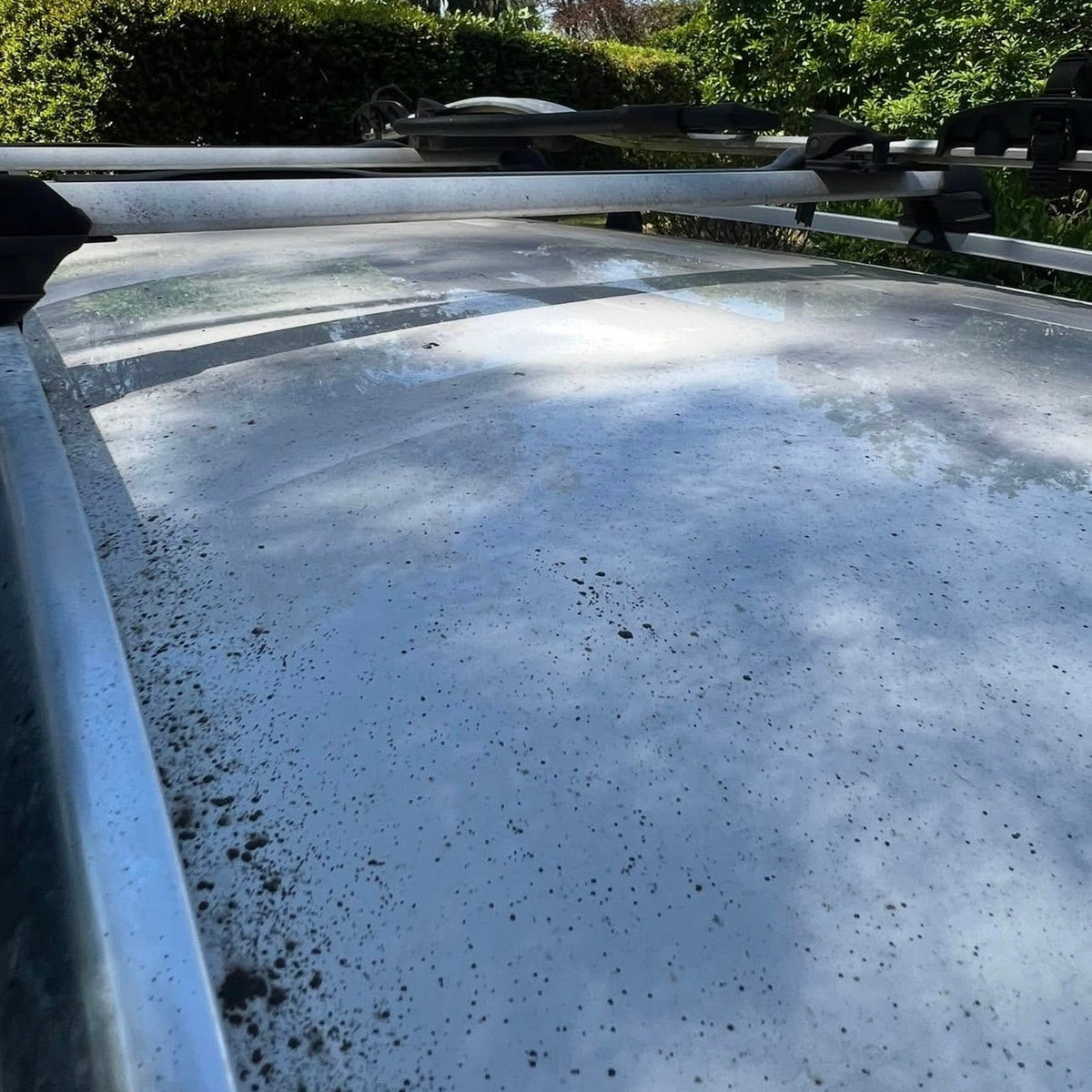 Before: white car roof covered in black spots and grime beneath the roof racks